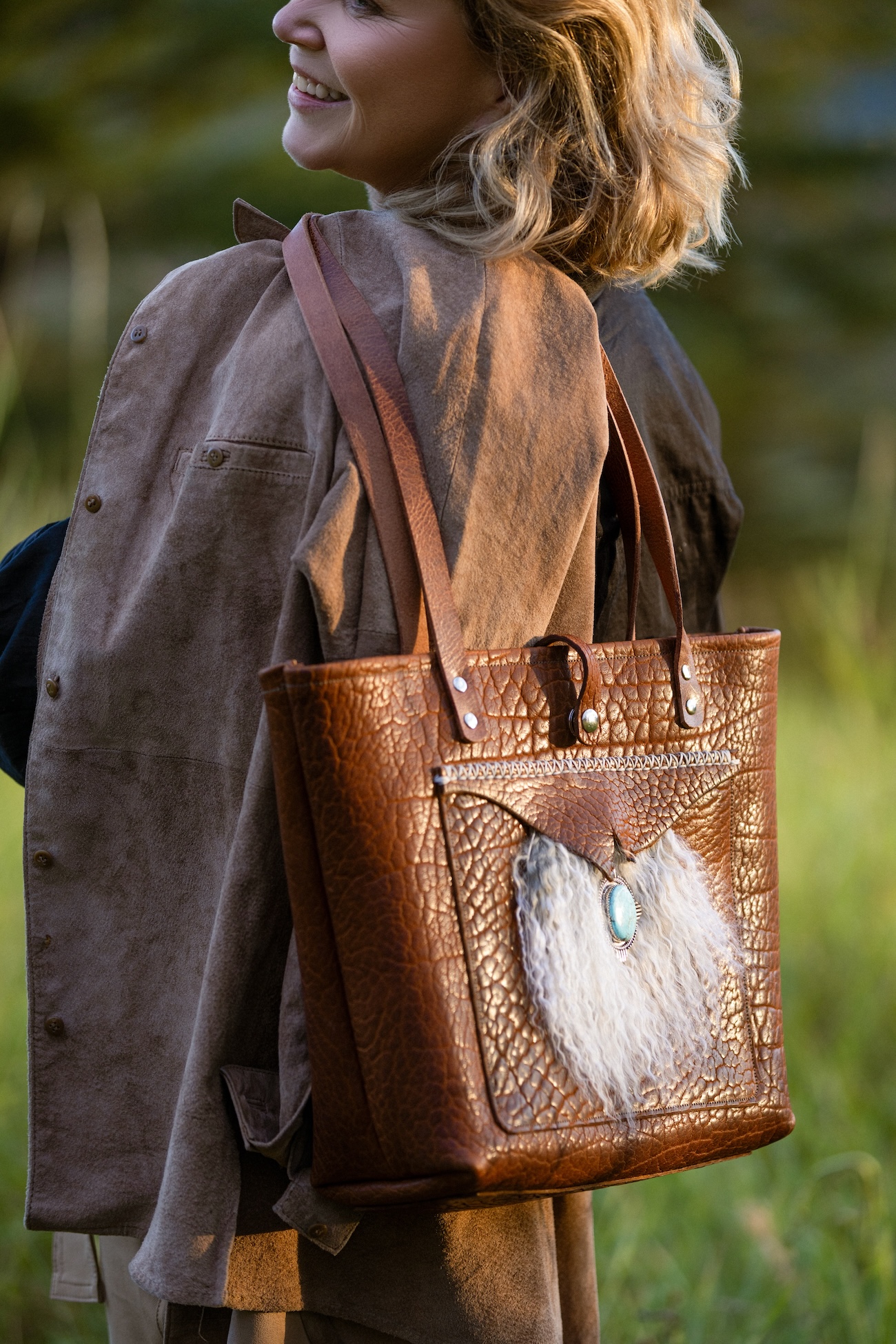 Artist and maker Jenny Keller with a tote bag made in bison leather and trimmed with lamb fur and a silver and turquoise medallion